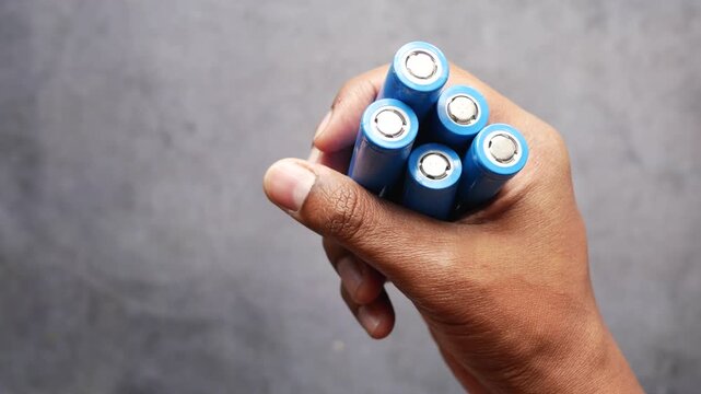 Close up of person hand holding five blue lithium ion rechargeable batteries on gray background