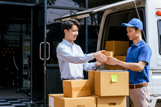 Delivery worker handing a box to a man beside a van loaded with parcels, with stacked packages and an open rear door for transport