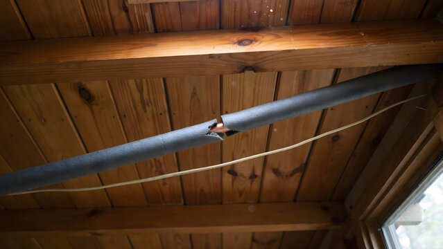 Damaged foam insulation on a copper water pipe under a wooden ceiling