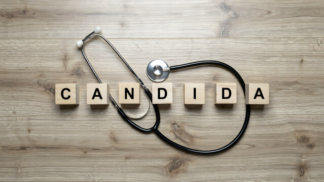 Medical stethoscope lying on wooden surface with wooden blocks spelling candida