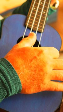 Hand ukulele strumming a man's hand playing a vibrant blue stringed music instrument. Vertical video.
