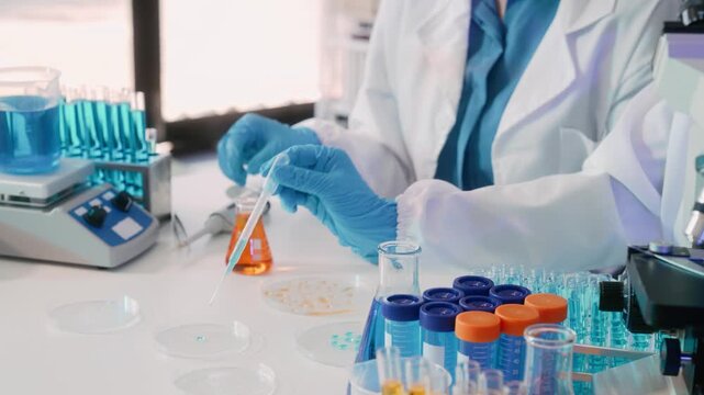 Scientist using pipette in a modern laboratory with test tubes, flasks and microscope, studying samples for medical analysis.