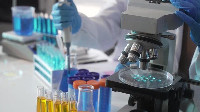Scientist using a microscope and pipette with test tubes and lab samples in a modern medical research laboratory