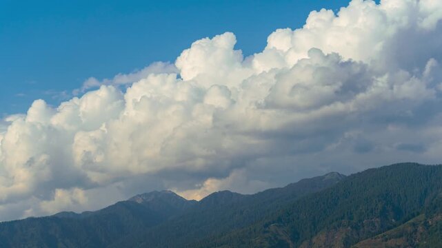4K Time lapse shot of clouds above the Himalayan mountain range with pine trees on top of it during the monsoon season as seen form Peej village near Kullu in Himachal Pradesh, India.