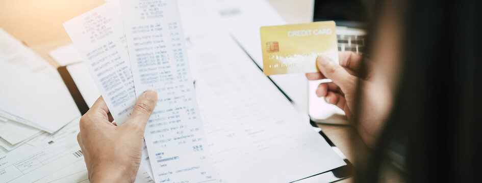 Close up medical financial banner of a woman hands holding credit card and high expense receipts for budget debt calculation at home