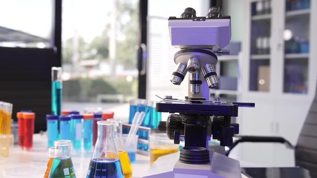 Microscope in a science lab with colorful test tubes and flasks on a workbench, showing research, testing and laboratory equipment.