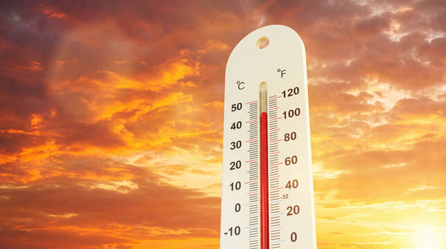 White vertical thermometer showing high temperature against a dramatic orange and red sky with clouds at sunset