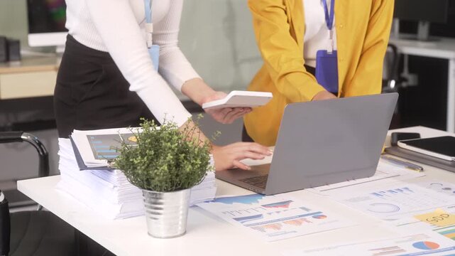 Two business colleagues review documents and charts beside a laptop in a modern office, showing teamwork, planning, and data analysis.