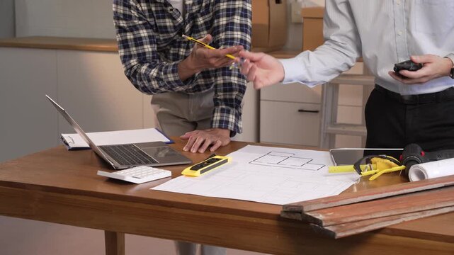 Two men reviewing house plans and measuring tools at a desk during a meeting