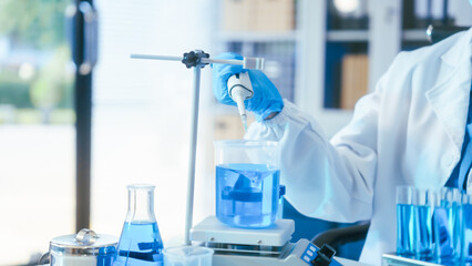 Fototapeta premium Scientist in lab coat and gloves using a pipette with blue liquid in a modern laboratory setting.