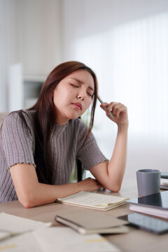 Young Asian woman feeling exhausted and stressed while working at home desk with notebook and coffee with copy space
