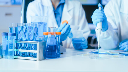 Fototapeta premium Scientists in a laboratory using a pipette with glass test tubes and blue liquid, showing medical research, testing and analysis.