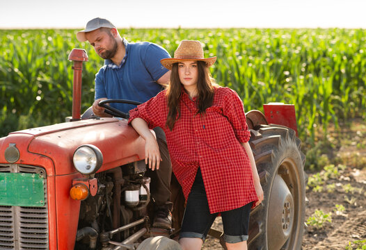 Young farmers with vintage tractor in corn field at sunset