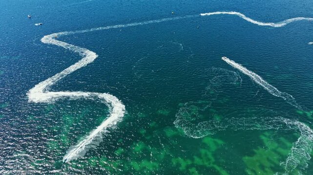 Jet skis race over clear water, leaving white trails behind as they make sharp turns. The event takes place during the day, with sunlight reflecting on the surface.