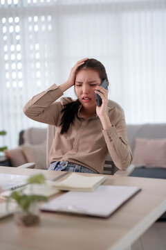 Stressed Asian businesswoman talking on phone while working at home office feeling overwhelmed and anxious with copy space
