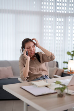 Stressed young Asian woman having difficult phone conversation while working from home experiencing emotional pressure with copy space