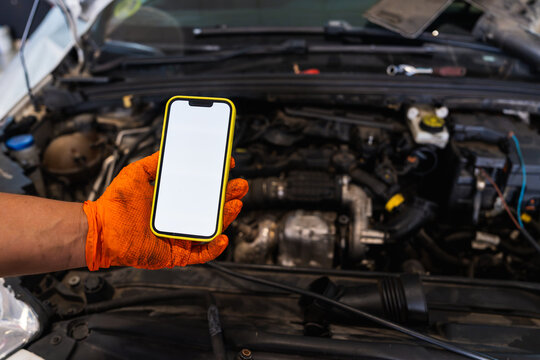 Mechanic hand holding smartphone with blank screen over car engine