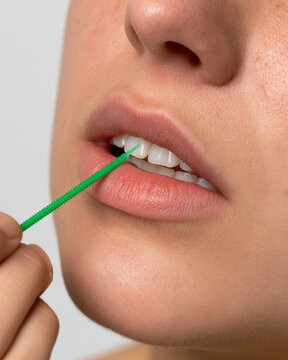 Close up of person using green interdental brush between front tooth, clean dental care, natural lip texture, smooth skin