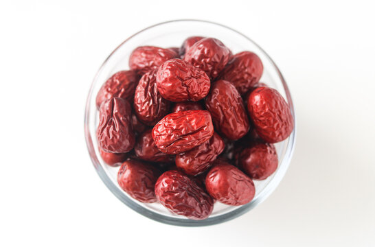 Top-down view of a transparent glass bowl filled with dried jujubes (Chinese red dates), showcasing their rich reddish color and natural texture.