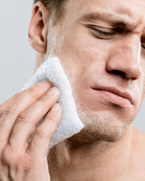 Man holding ice pack on cheek facial pain cold compress jawline care close up clean background natural stubble discomfort skincare treatment