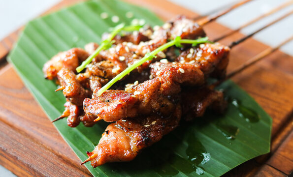 Grilled pork belly skewers served on a banana leaf atop a wooden board.