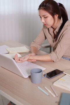 Young Asian woman experiencing work stress while typing on laptop at minimalist home office desk with copy space