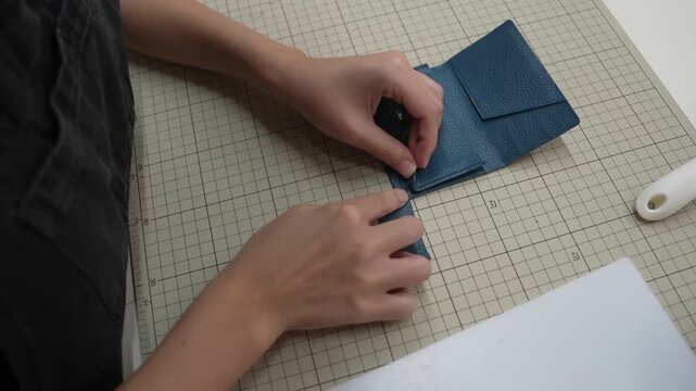 Hands attach small leather tab piece to wallet flap