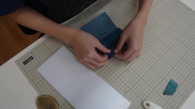 Craftsperson folds leather flap over wallet body aligning edges