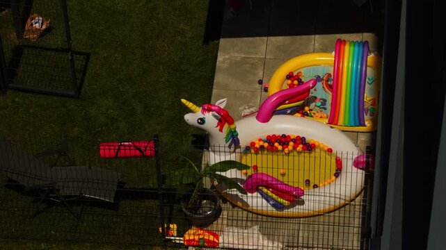 A colorful inflatable unicorn pool float sits beside a small children&rsquo;s splash pool with bright toys in a sunny backyard. Ideal for summer, family, outdoor recreation, and childhood concepts.