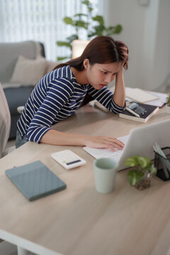 Stressed young Asian woman holding head in frustration while working on laptop at home office desk with copy space