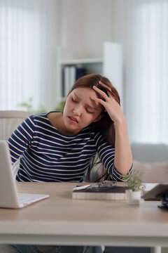 Young Asian woman experiencing work stress and headache while working from home office with copy space