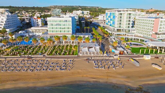 Aerial view of Protaras beach resort in Cyprus. Sandy beach, sunbeds, palm trees, swimming pools and beachfront hotels create a sunny Mediterranean holiday scene.