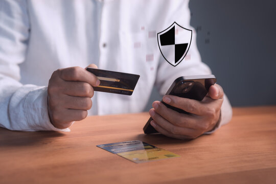 Man using smartphone and credit card for secure online payment. The virtual shield icon represents cyber security, safe mobile banking, finance protection, and trusted e-commerce transactions.