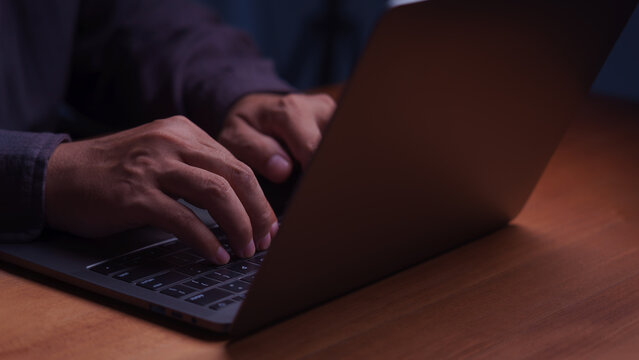 Close up of male hands typing on a laptop computer keyboard at night. Working late on modern business technology, internet connection, remote work, and online digital network communication.
