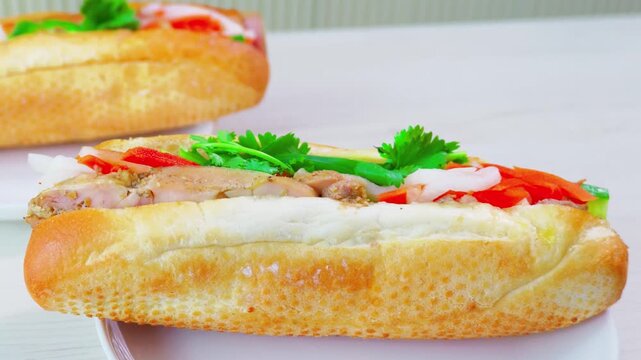 Pair of authentic Vietnamese banh mi sandwiches rest on clean white plates over a bright neutral surface.