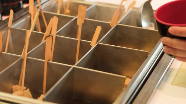 Customer Pointing at Korean Fish Cake Skewers in Hot Broth