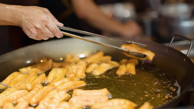 Chef Frying Traditional Asian Dough Sticks in Large Wok with Tongs