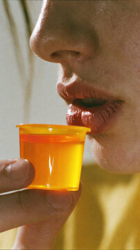 Lip mouth syrup cup medicine dose liquid orange health throat chapped natural skin closeup profile female face hand fingers translucent plastic clear sunlight soft blur background macro side view
