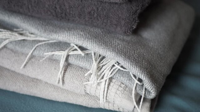 Stack of folded warm blankets and soft towels with fringe detail in calm gray and beige tones for home comfort