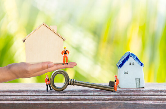 Miniature house with miniature worker and key over blurred green leaves background, property and real estate industry