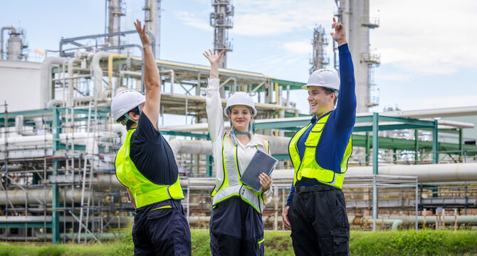 industrial engineering team raising hands in celebration at oil refinery plant, successful professional workers and engineers cheering together at petrochemical facility