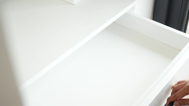 A person opening and closing a white desk drawer with gold and black handles in a bright room
