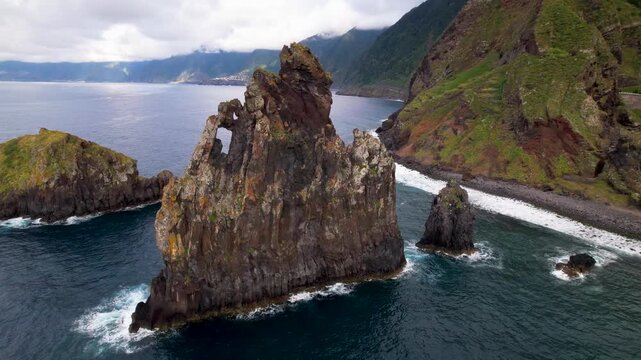 Ribeira da Janela Madeira Portugal Aerial Drone Low Angle Orbit Around Volcanic Sea Stack Rock with Natural Hole Revealing Narrow Rock Profile Pebbled Beach and Mountains Travel Video 4K UHD