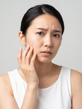Worried young Asian woman touching her face looking concerned about skin problems and wrinkles