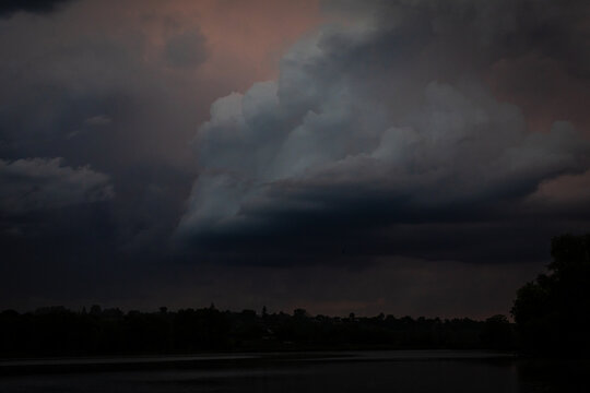 A massive low cloud sweeps across twilight skies casting deep shadow over the reservoir while faint warm light lingers at the edge evoking the powerful mood of passing storms