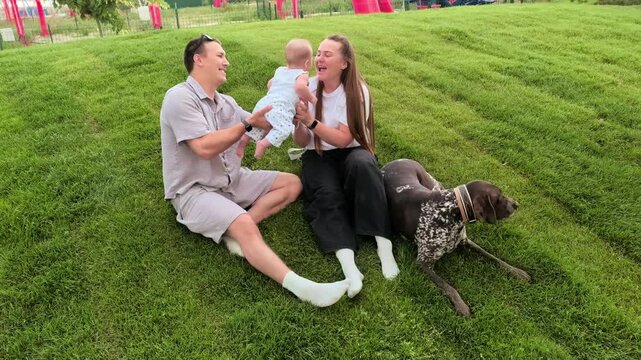 Young parents relax with their infant and dog on green grass outdoors, loving family bonding, pet companionship, peaceful summer lifestyle.