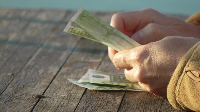 Money Euro Counting Hands quickly shuffle and count hundred euro banknotes on a rustic outdoor wooden table.