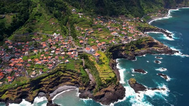 Seixal village Madeira Portugal 4K Drone. Top down view over natural swimming pools and ocean
waves on rugged coast. Cloud covered green mountains slow flight. 
cinematic footage