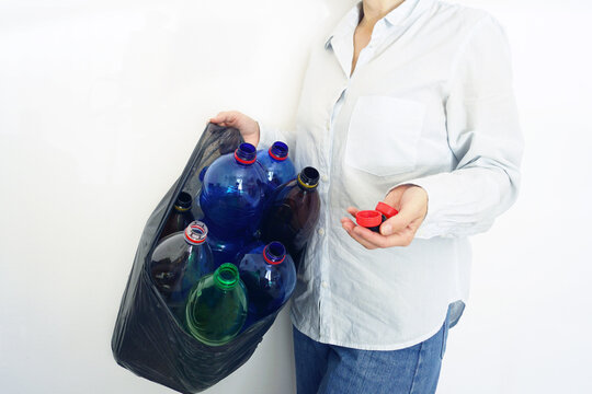 Woman carries black garbage bag filled with empty plastic bottles while holding bottle caps in her palm. Represents recycling preparation, deposit return systems, and environmental responsibility.