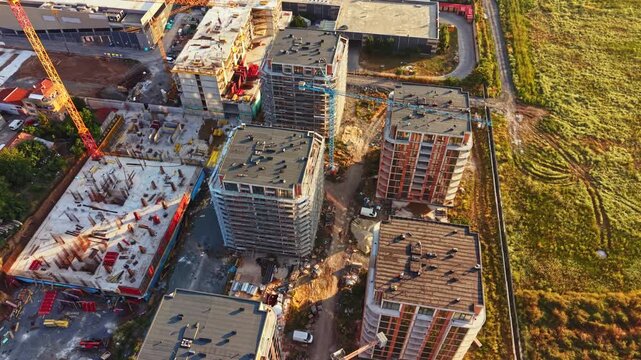 Workers are busy at a construction site where multiple buildings are being erected. Equipment and materials are scattered around the area.